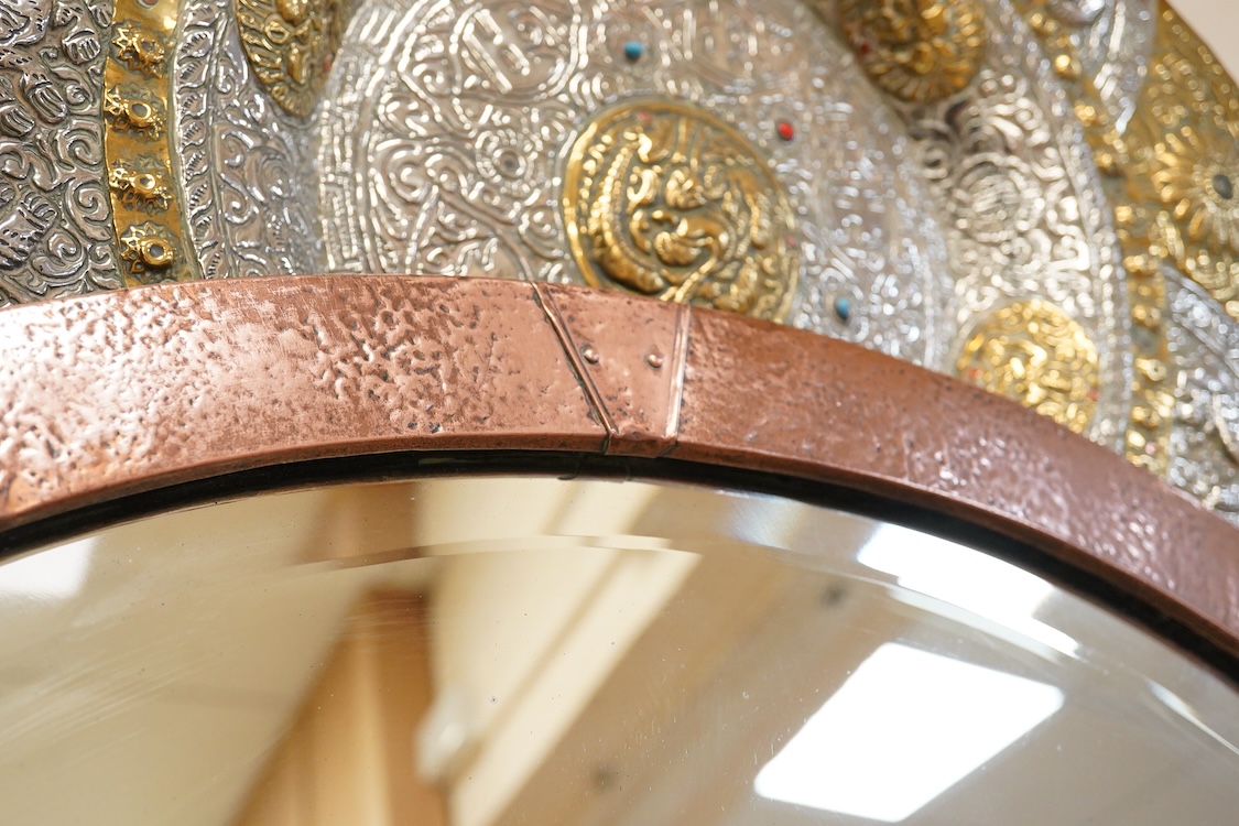 An oval late 19th century hammered copper wall mirror with rams head cartouches, 65cm wide